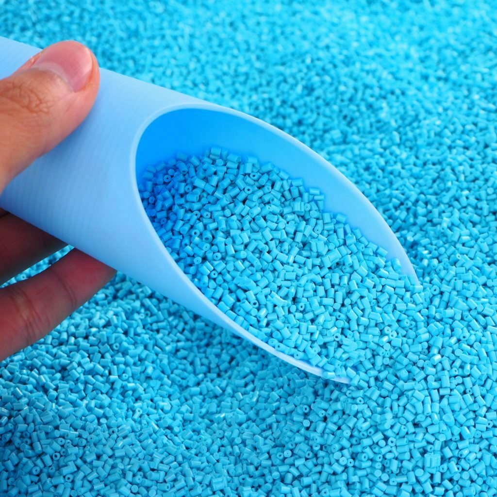Raw Material Of Plastic Bead. Close-up Hand And Sample Size. Recycled polymer beads in light blue color